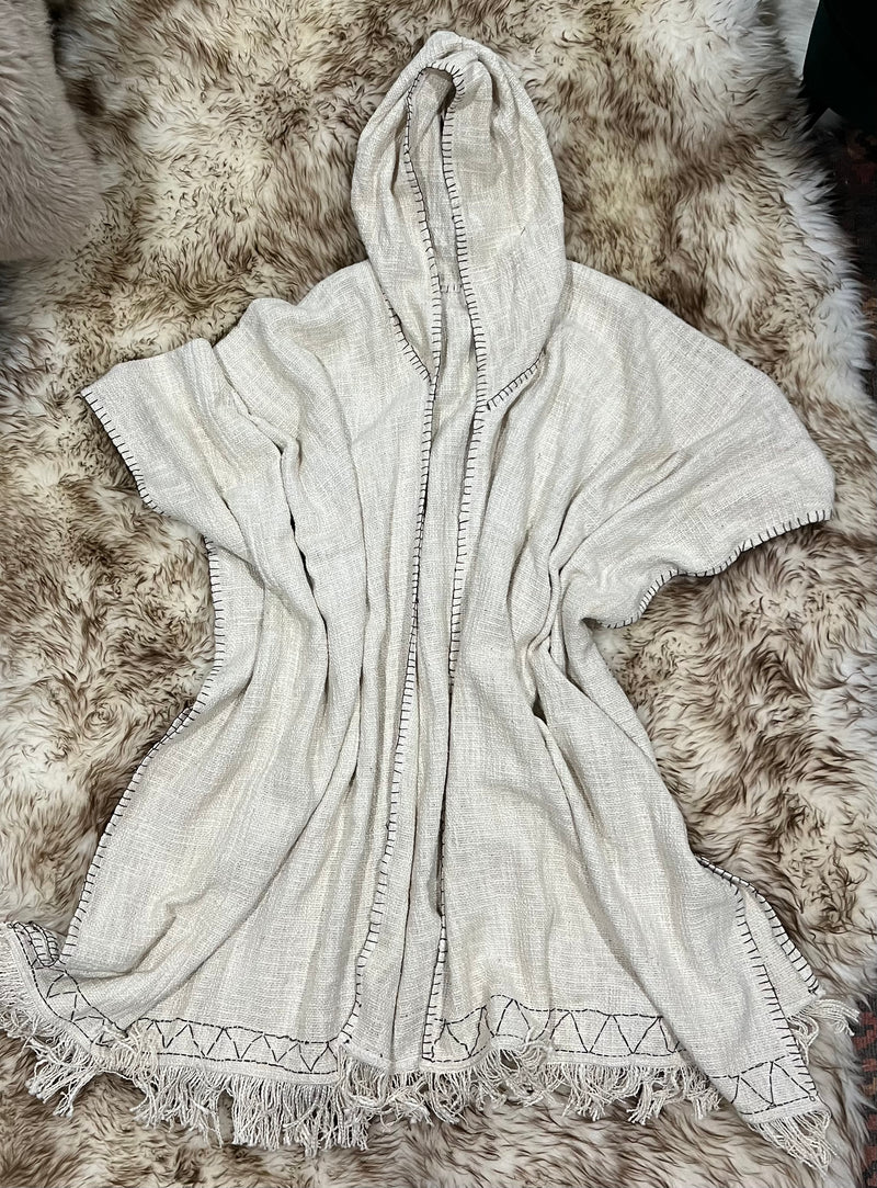 "Hand-embroidered cream-colored cotton poncho with hood, featuring frayed edges and intricate brown embroidery, perfect for casual outings or cozy evenings."