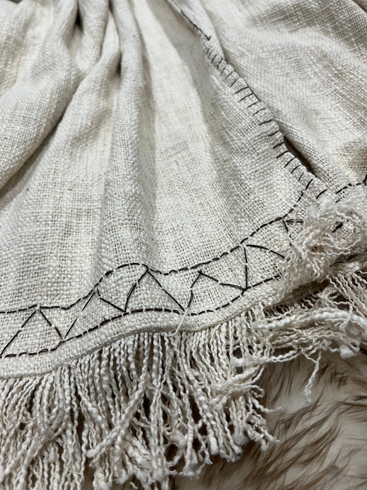 "Hand-embroidered cream-colored cotton poncho with hood, featuring frayed edges and intricate brown embroidery, perfect for casual outings or cozy evenings."